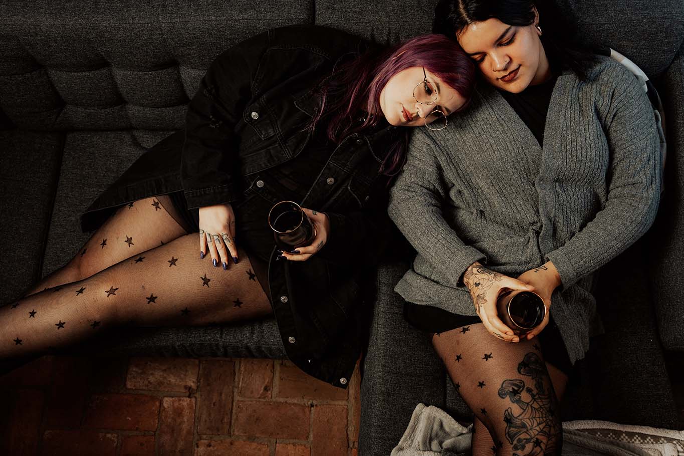 Feinstrumpfhose mit Sternchenmuster an den Beinen zweier Frauen, die aneinander angelehnt auf dem Sofa liegen und ein Glas in der Hand halten.